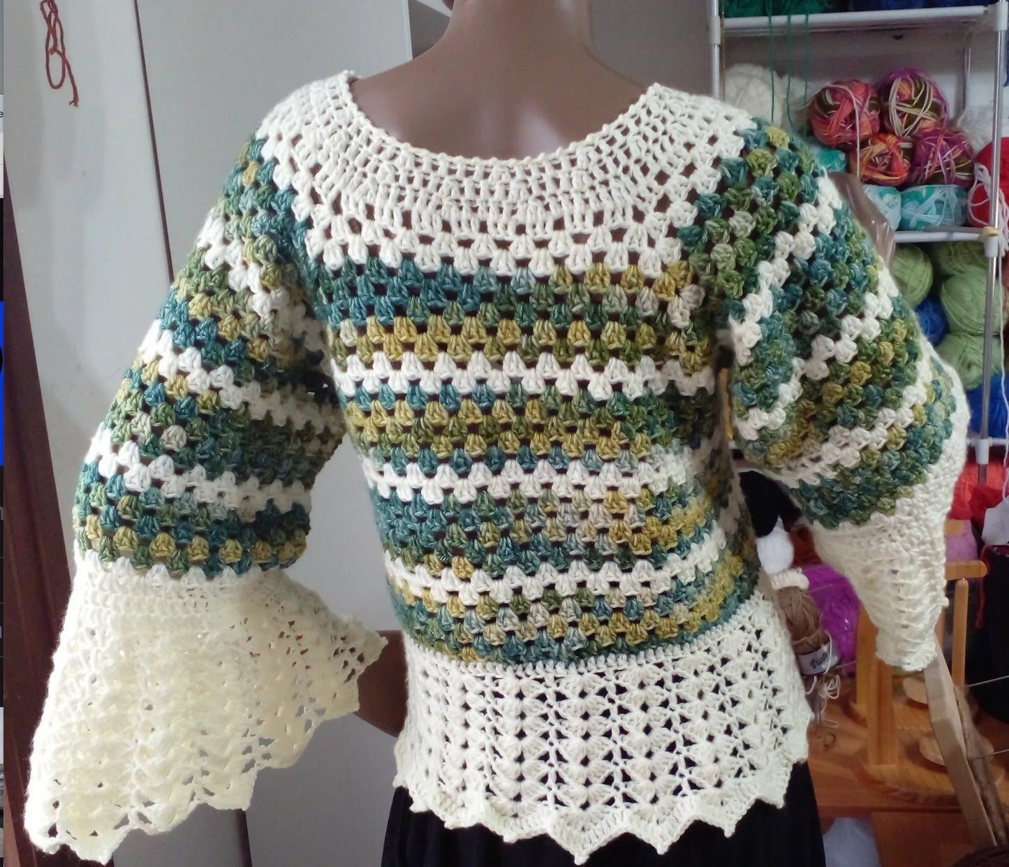 Pull au crochet Verduro de Cachalabibi -vue de dos dans l'atelier avec pelotes de laine colorées et étagères