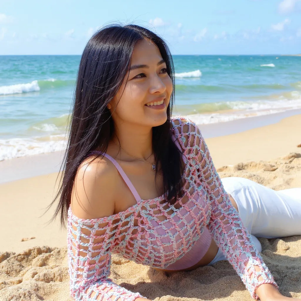 Crop top au crochet Bubblestar de Cachalabibi - vue de dos assise sur le sable doré avec une mer turquoise