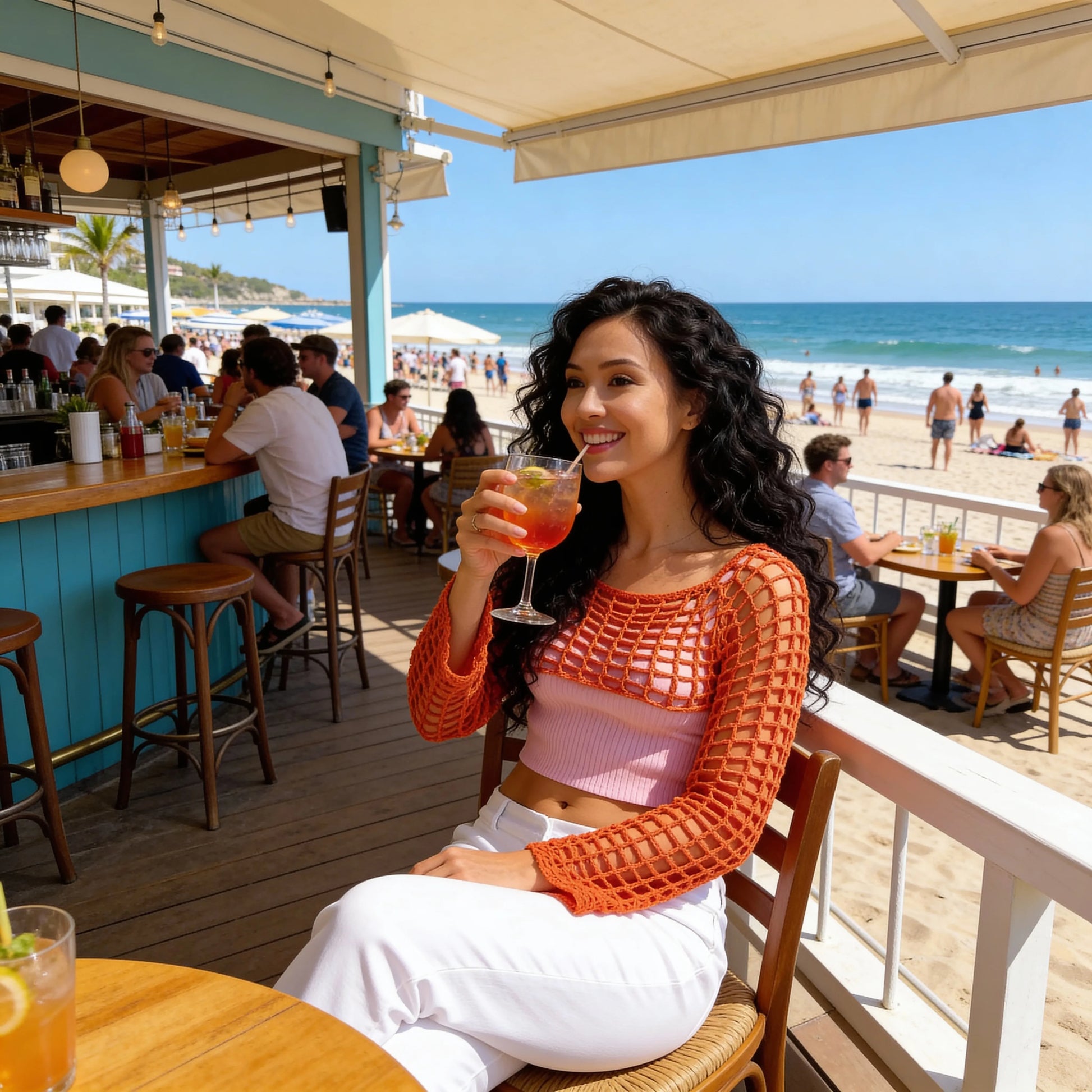 Crop top au crochet Hibisca de Cachalabibi - vue de face à la terrasse d'un bar de plage animé avec cocktail