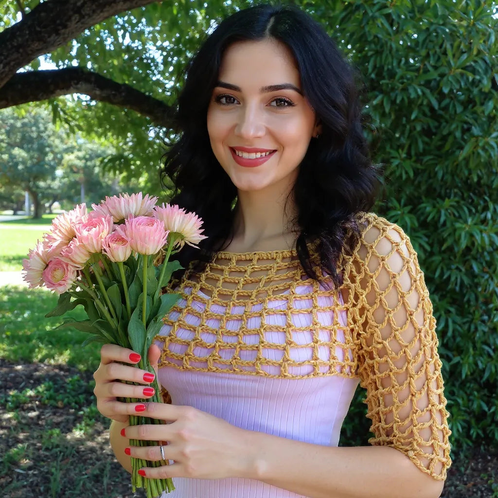 Crop top au crochet Sweetie de Cachalabibi - vue de face dans la nature verdoyante avec bouquet de fleurs roses