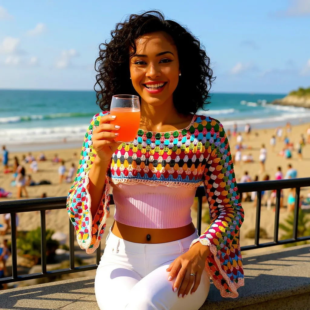 Crop top au crochet Volarino de Cachalabibi - vue de face au balcon avec cocktail orange face à la plage animée