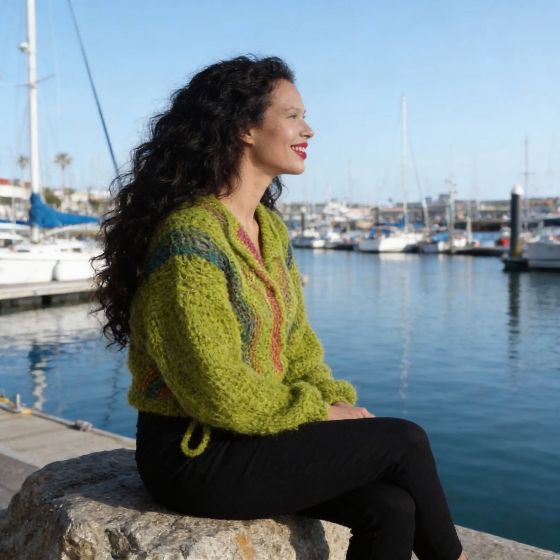 Gilet au crochet Avocado de Cachalabibi - vue de profil assise sur un muret à la marina avec voiliers et bateaux