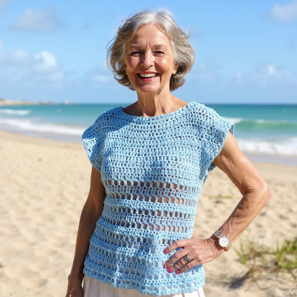 Haut au crochet Brunnera de Cachalabibi - vue de face d'une dame âgée posant sur  la plage devant une mer turquoise