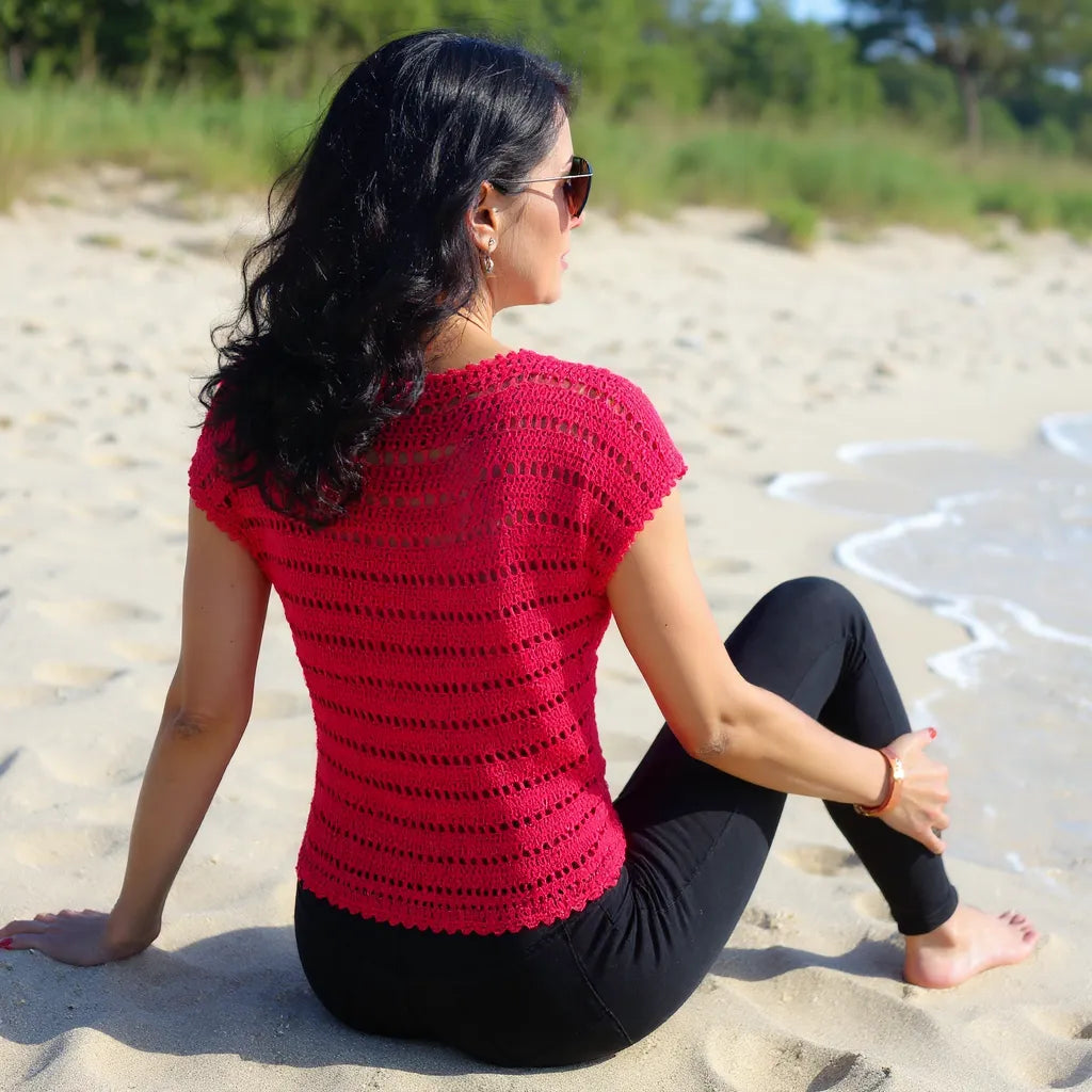 Haut au crochet Granada de Cachalabibi - vue de dos d'une femme assise à la plage près de la mer