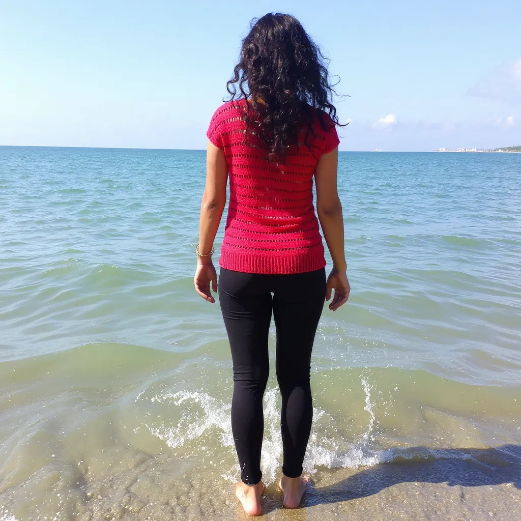 Haut au crochet Granada de Cachalabibi - porté debout à la plage par une femme avec les pieds dans l'eau