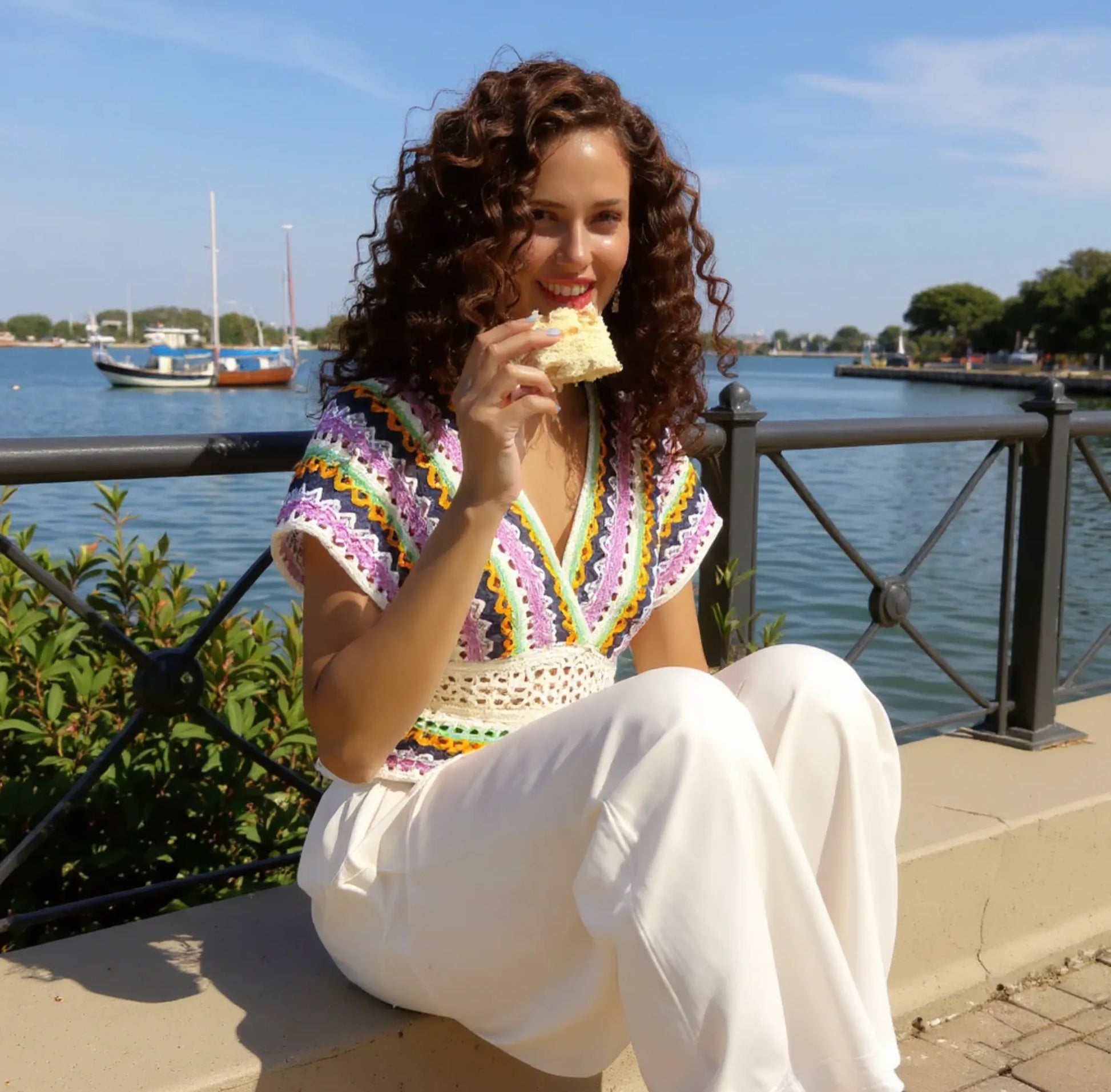 Haut au crochet Mayabella de Cachalabibi - vue de face d'une jeune fille assise qui mange un gâteau devant la mer