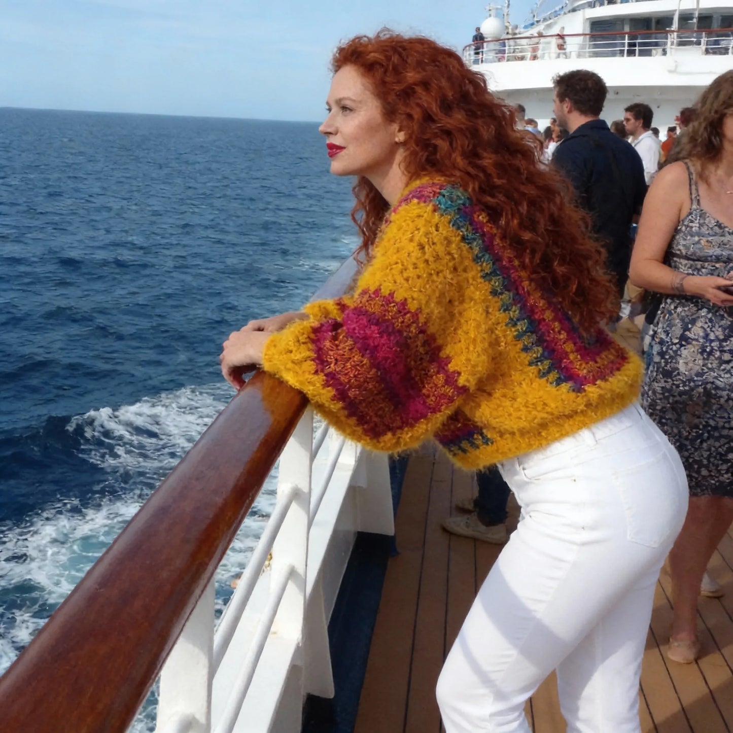Poncho au crochet Aranciano de Cachalabibi - vue de profil sur le pont d'un bateau de croisière avec l'océan et des passagers
