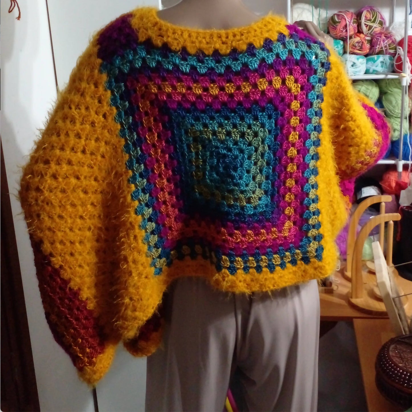 Poncho au crochet Aranciano de Cachalabibi - vue de dos dans l'atelier avec pelotes de laine colorées et étagères