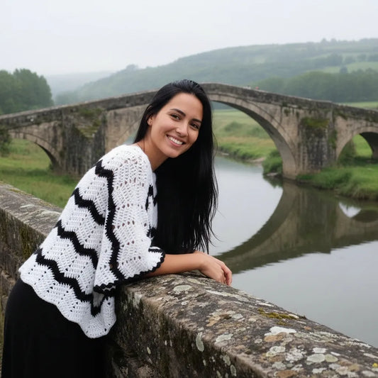 Poncho au crochet Bianconero de Cachalabibi - vue de face sur un pont en pierre avec rivière et collines verdoyantes
