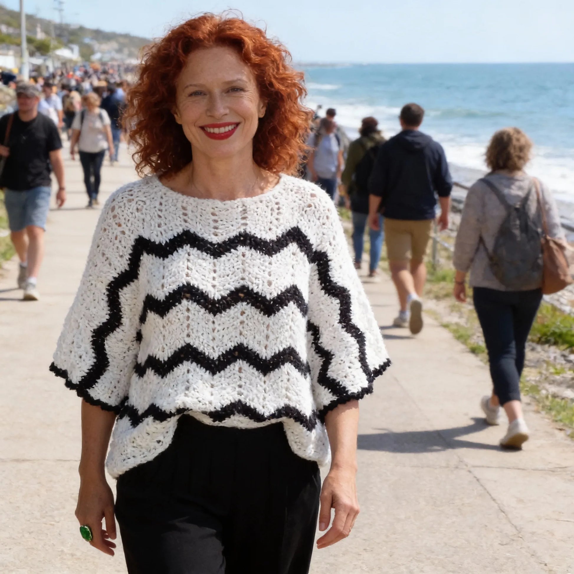 Poncho au crochet Bianconero de Cachalabibi - vue de face sur une promenade en bord de mer avec plage et promeneurs