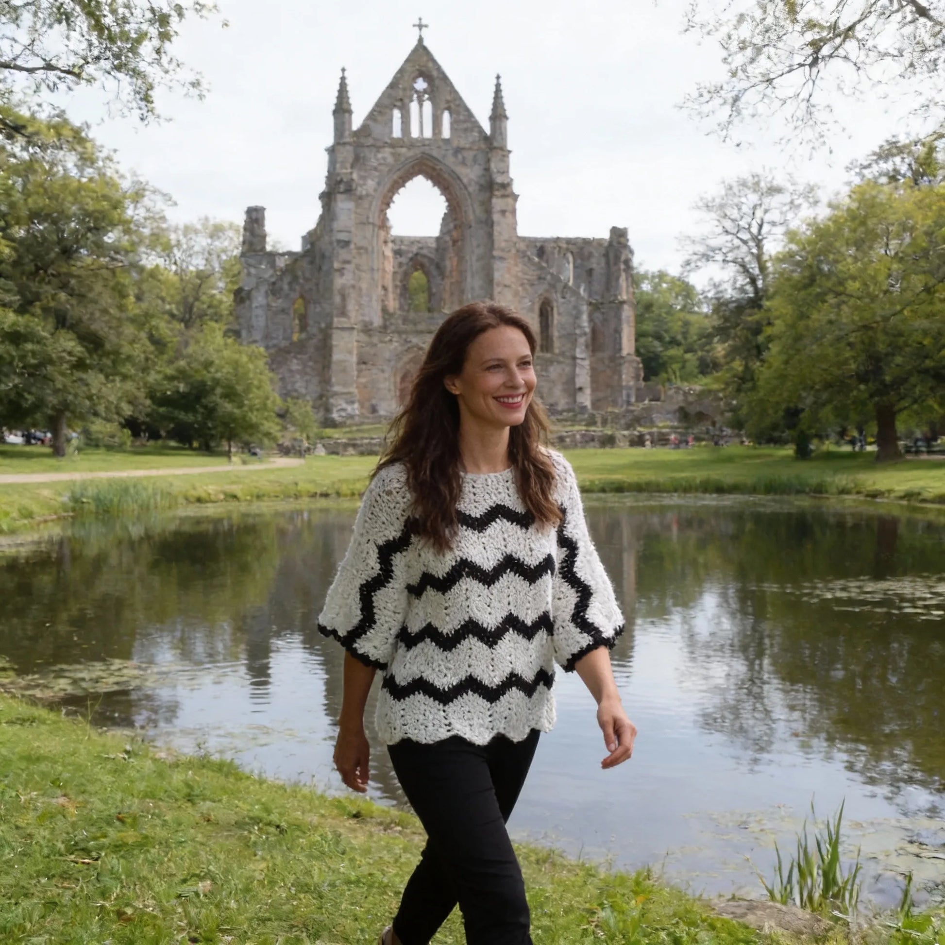 Poncho au crochet Bianconero de Cachalabibi - vue de face devant une abbaye en ruines avec étang et verdure