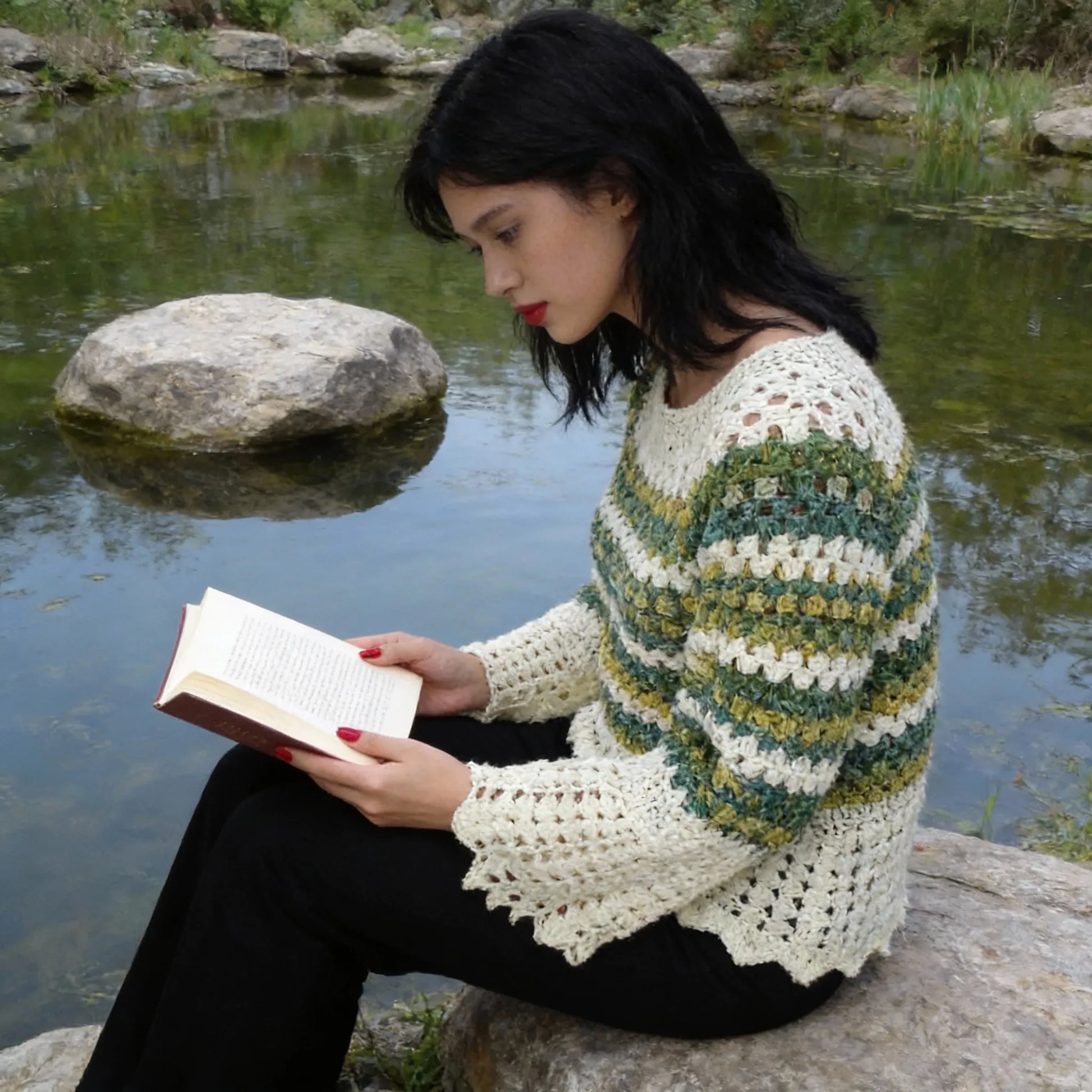 Pull au crochet Verduro de Cachalabibi -vue de profil au bord d'un étang avec rochers et eau calme lisant un livre