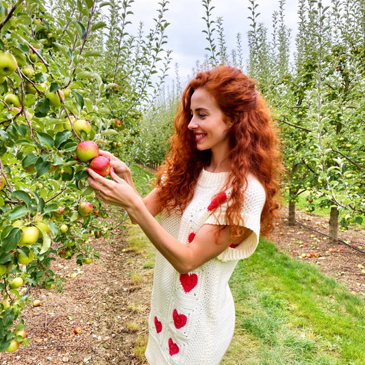 Robe au crochet Dressy de Cachalabibi -vue de face dans un verger de pommiers avec panier de pommes et rangées d'arbres
