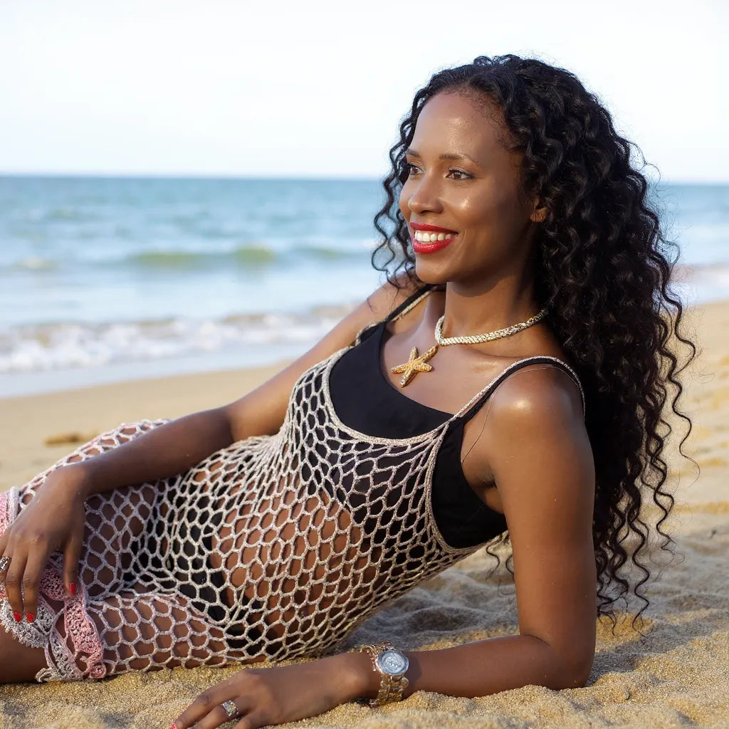 Robe de bain au crochet Bellarete de Cachalabibi - vue de profil assise sur le sable à la plage turquoise