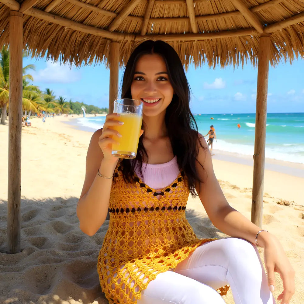 Robe de bain au crochet Cocconoce de Cachalabibi - de face une jeune femme qui boit un jus d'orange sous une paillotte
