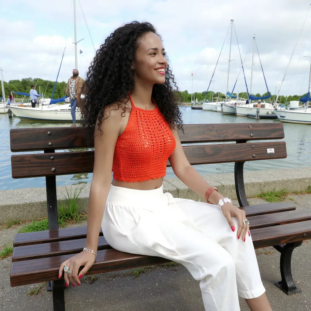 Top dos nu au crochet Calendula de Cachalabibi - vue de côté d'une jeune femme aux longs cheveux noirs bouclés assise sur un banc dans une marina